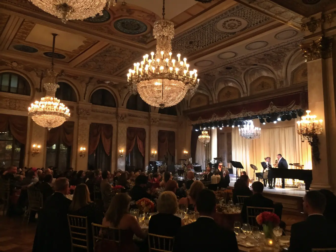 A lively scene of a cultural evening event at the château, with people enjoying music, art displays, and regional cuisine in a warmly lit historic hall.